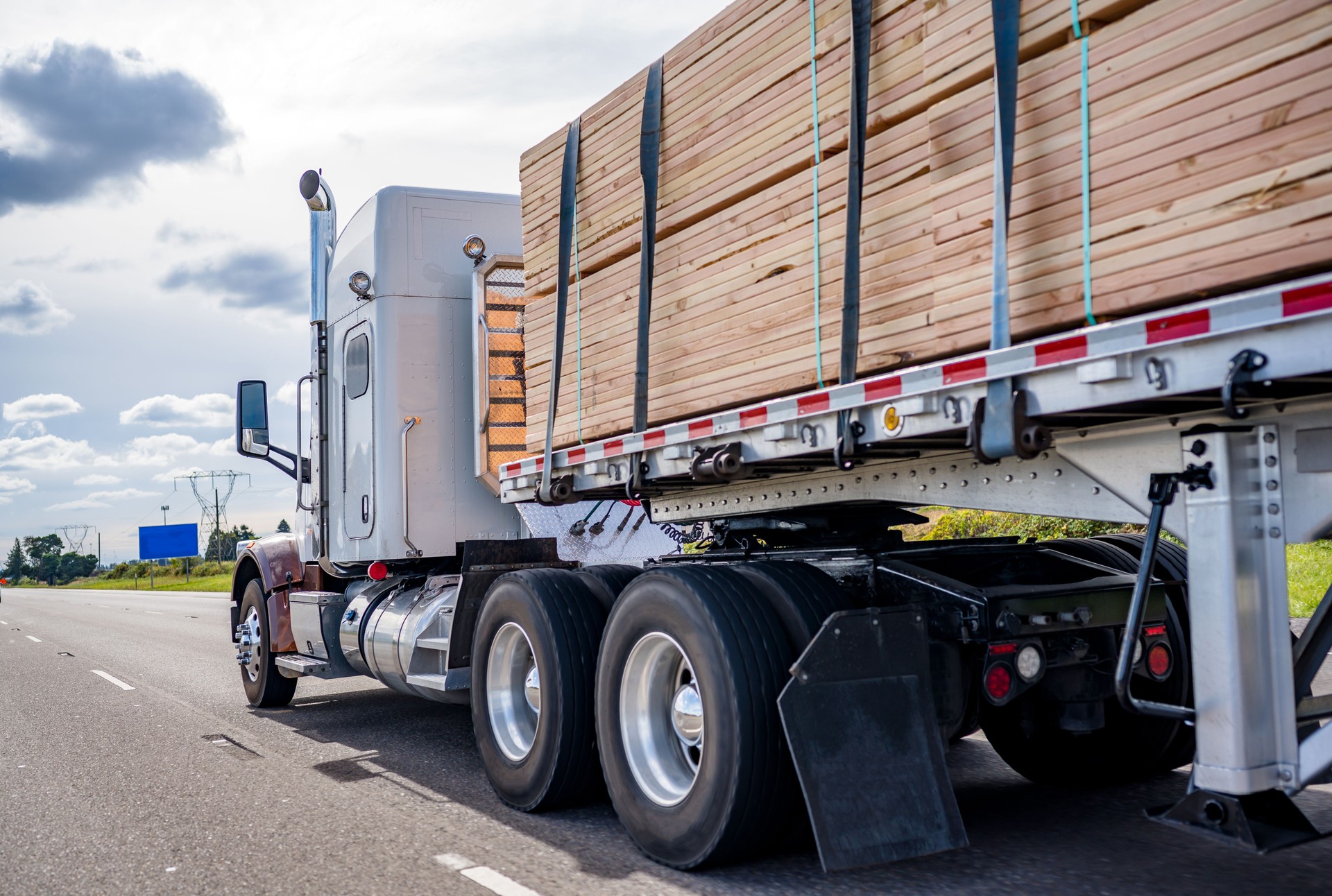 Classic big rig semi truck tractor transporting lumber on the flat bed semi trailer moving on the wide highway road